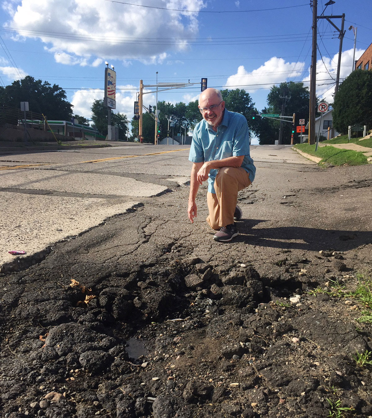  Jeffrey Dains kneeling next to a section of damaged road on Eustis Street